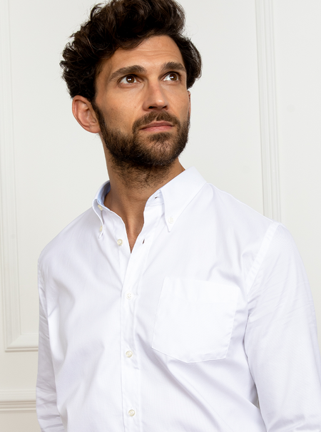 Man wearing white long sleeved shirt with button down collar and the inside collar and cuffs trimmed with sky blue. Made with 100% cotton in Thomas Mason fabric.